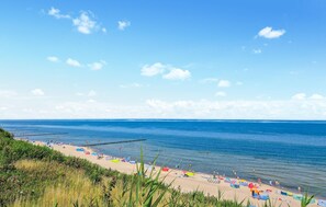 Ein Strand mit klarem, blauem Wasser, einem sandigen Ufer und einem Steg, der sich ins Meer erstreckt.