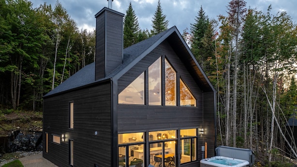 Una cabaña moderna con un gran ventanal, mobiliario exterior y un jacuzzi.