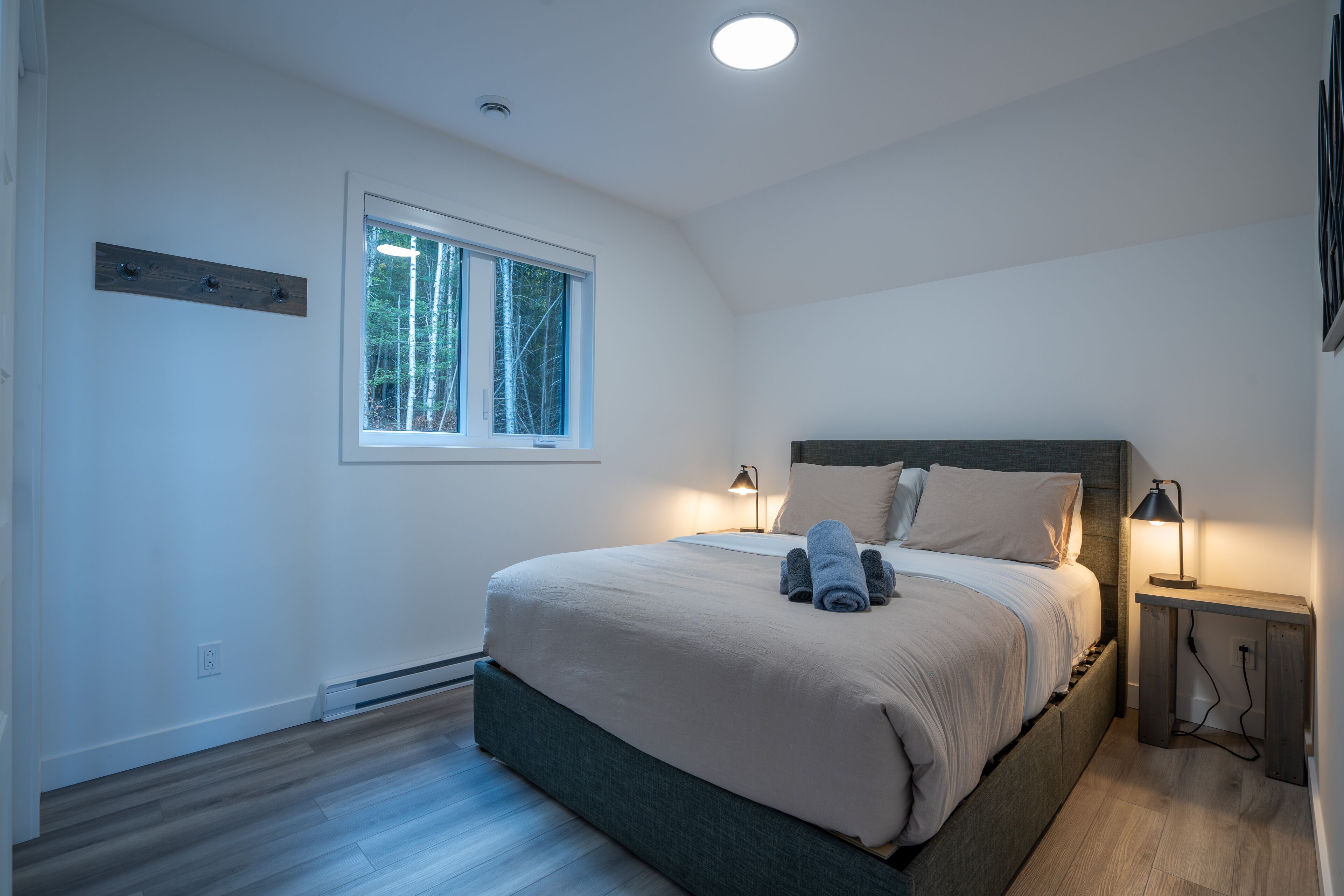 Un dormitorio con cama, lámparas de noche, una ventana y suelo de madera.