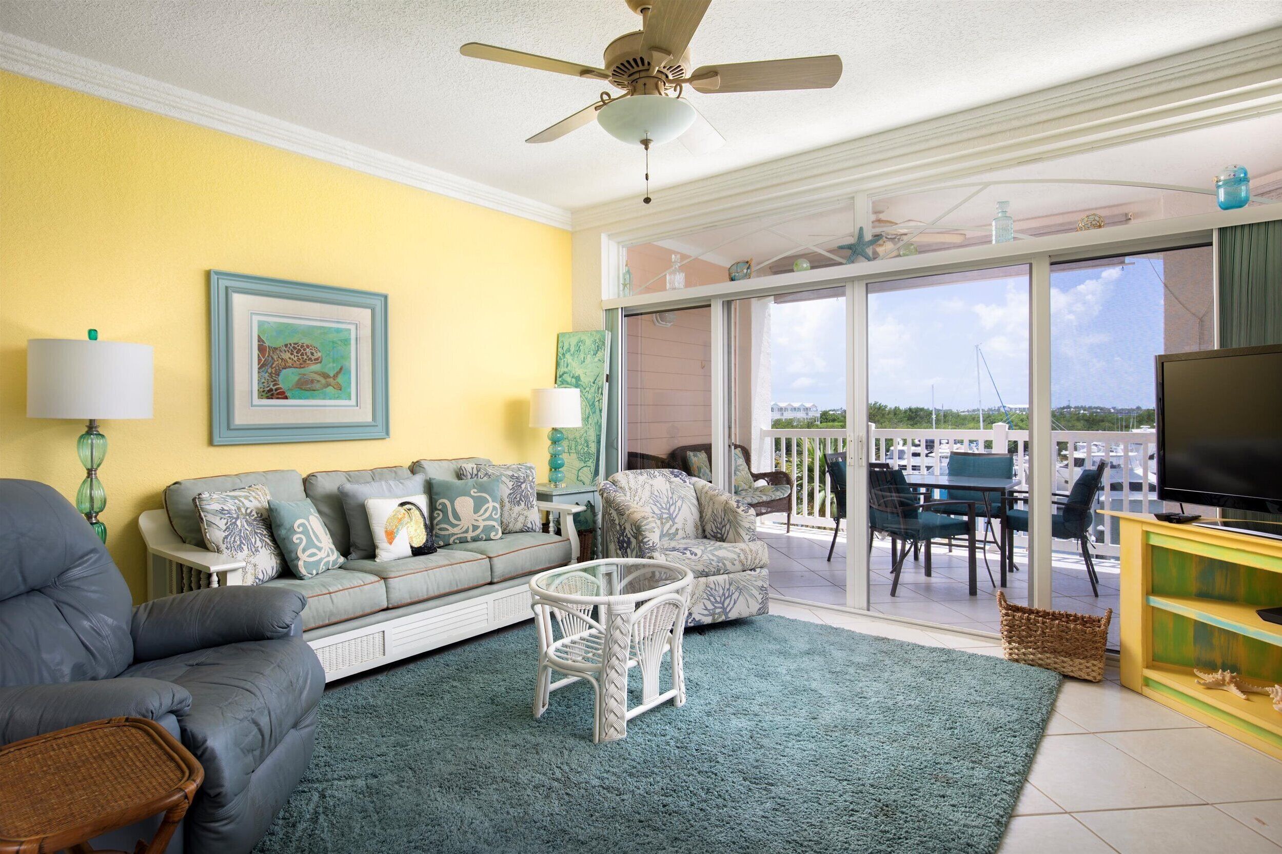 A living room with a sofa, armchair, and a small table. There is a TV on a stand and a ceiling fan.