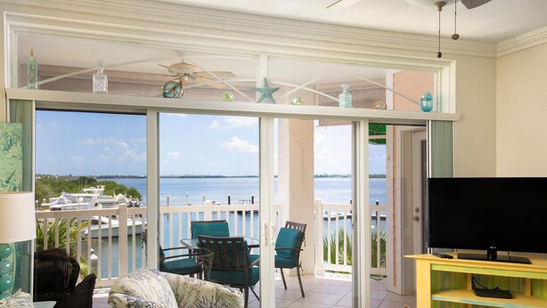 Un salon équipé d’un téléviseur, d’un canapé et d’un balcon offrant une vue sur l’eau.