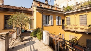 Une cour avec un arbre, des plantes en pot et un banc.