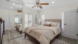 A bedroom with a bed, a ceiling fan, a mirror, and a door.
