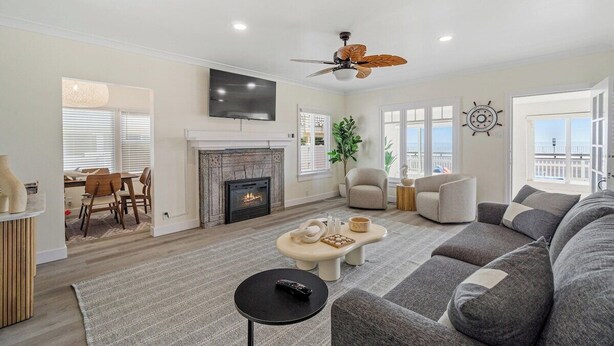 A living room with a fireplace, a ceiling fan, a TV mounted on the wall, and a large window with a view.