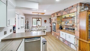 A kitchen with a wooden countertop, a dishwasher, a brick wall, and a dining area with chairs and a table.