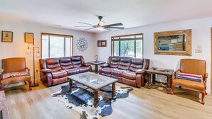 A living room with leather sofas, a glass coffee table, and a ceiling fan.