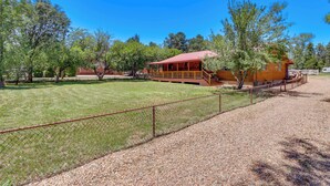 A wooden cabin with a red roof, surrounded by a gravel driveway and a chain-link fence.
