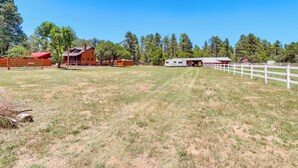 A ranch-style building with a large open field, fenced areas, and a white fence line.