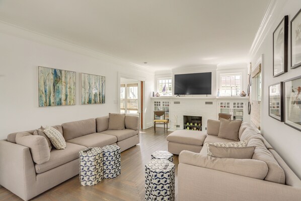 A spacious living room with a beige sofa set, patterned ottomans, a flat-screen TV, and a fireplace. - Port Clinton Home w/ Lake View - Walk to Beach! (Port Clinton)