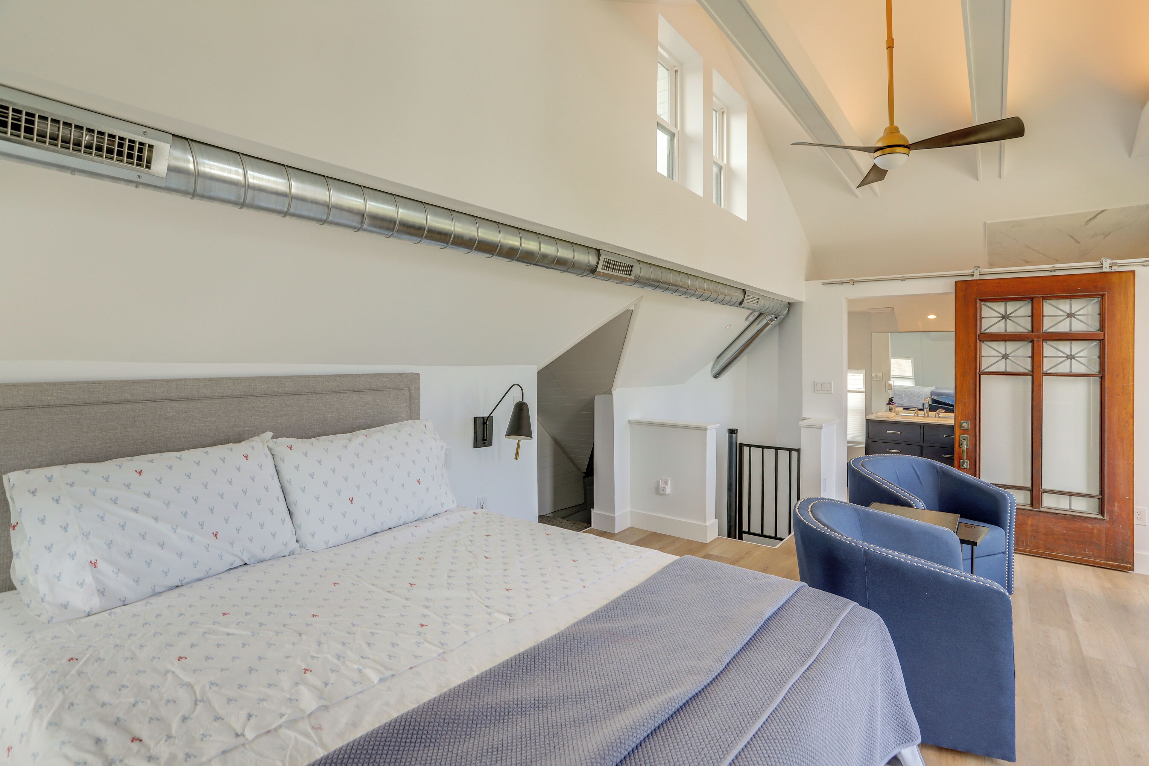 Une chambre à coucher avec un grand lit, un bureau, une chaise, un ventilateur de plafond et un escalier.