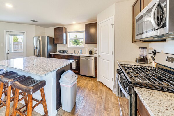 A modern kitchen with a granite countertop, stainless steel appliances, and wooden stools. - San Antonio Home w/ Pool Access: 11 Mi to Seaworld (San Antonio)
