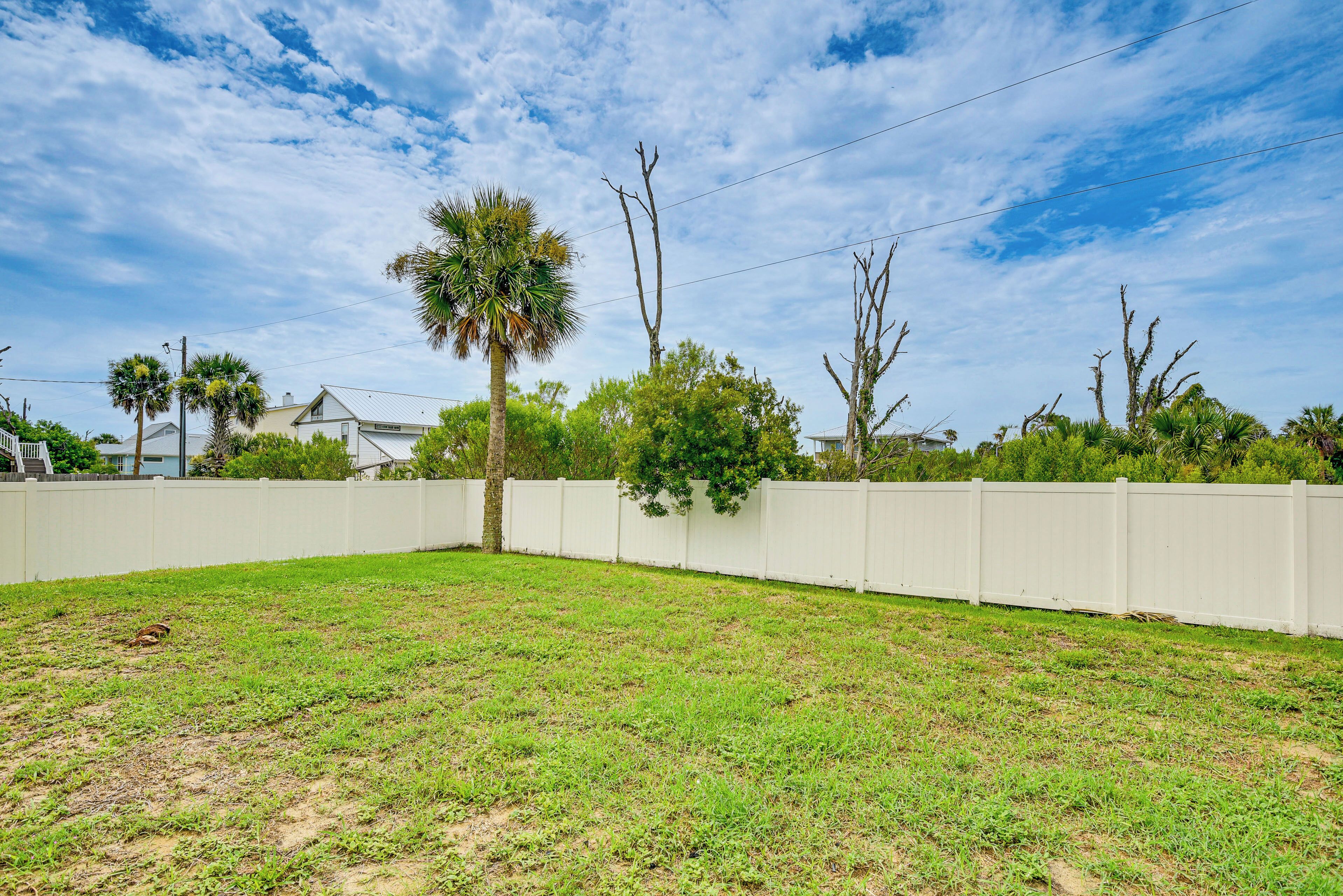 A grassy backyard with a white fence, trees, and a clear sky.