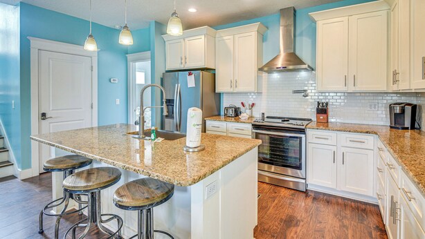 A kitchen with white cabinets, a granite countertop, stainless steel appliances, and a central island with stools. - Close to Beaches: Palm Coast Home w/ Deck! (Palm Coast)