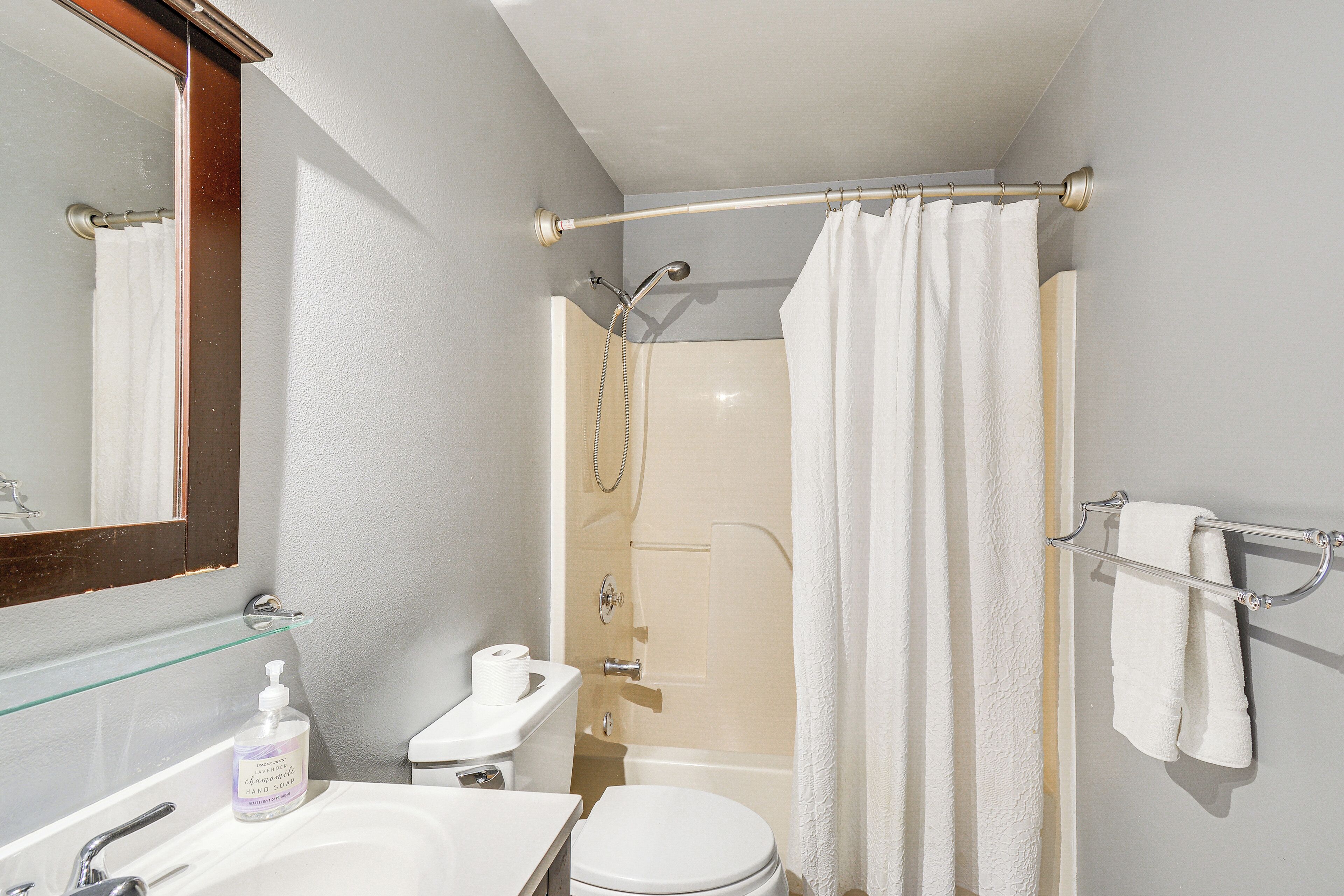 A bathroom with a shower, toilet, sink, and a mirror.