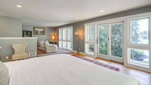 A spacious bedroom with a large bed, a chair, a desk, and a view through large windows. - Bayfront PNW Lodge: Dock, Pickleball & Guest House (Bainbridge Island)