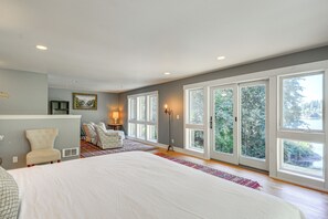 Une chambre spacieuse avec un grand lit, une chaise, un bureau et une vue dégagée grâce à de grandes fenêtres.