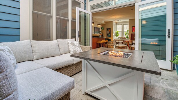 A cozy outdoor seating area with a cushioned sofa and a wooden table with a fire feature.