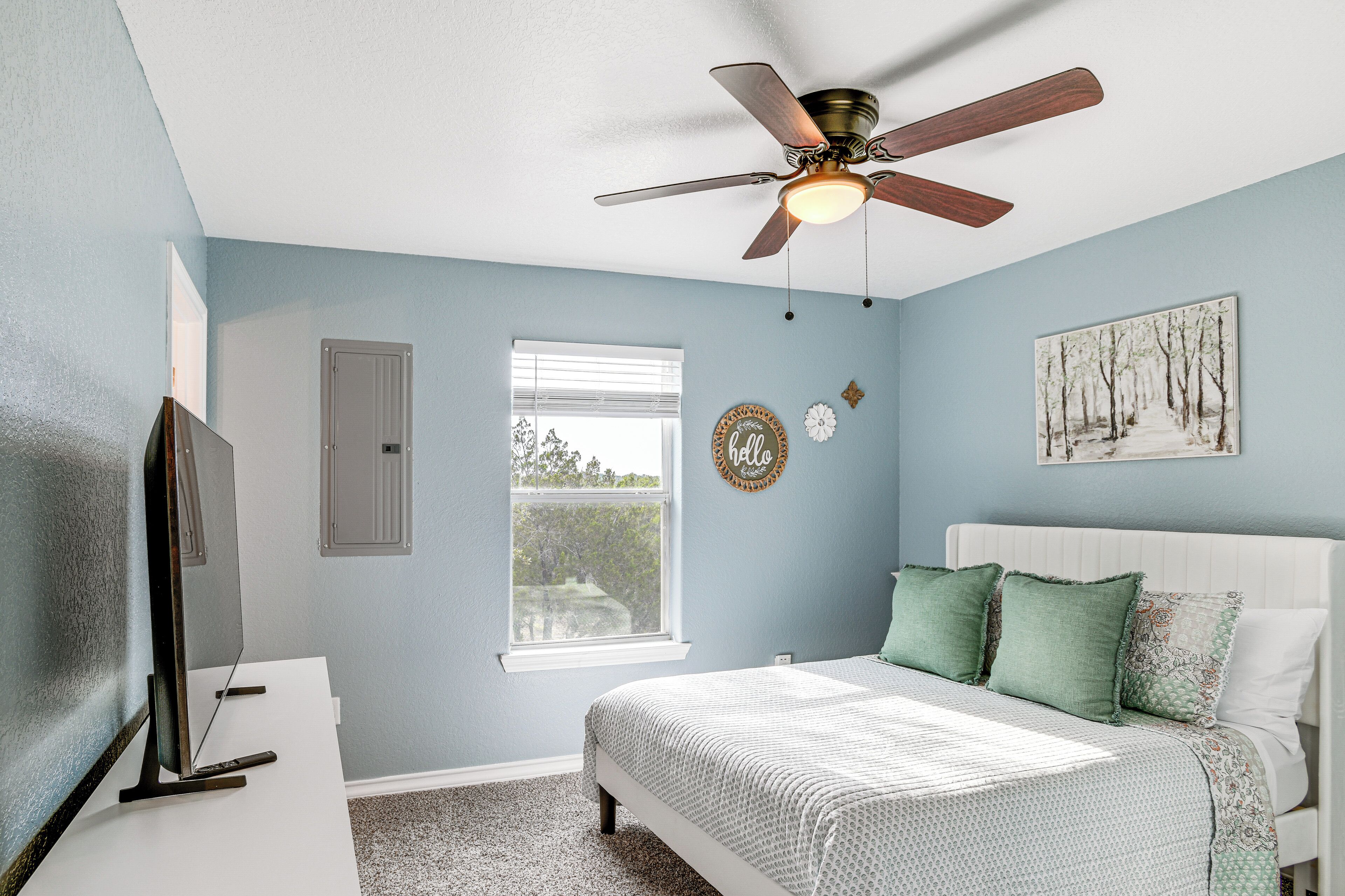 A bedroom with a bed, a ceiling fan, a window, and a painting on the wall.
