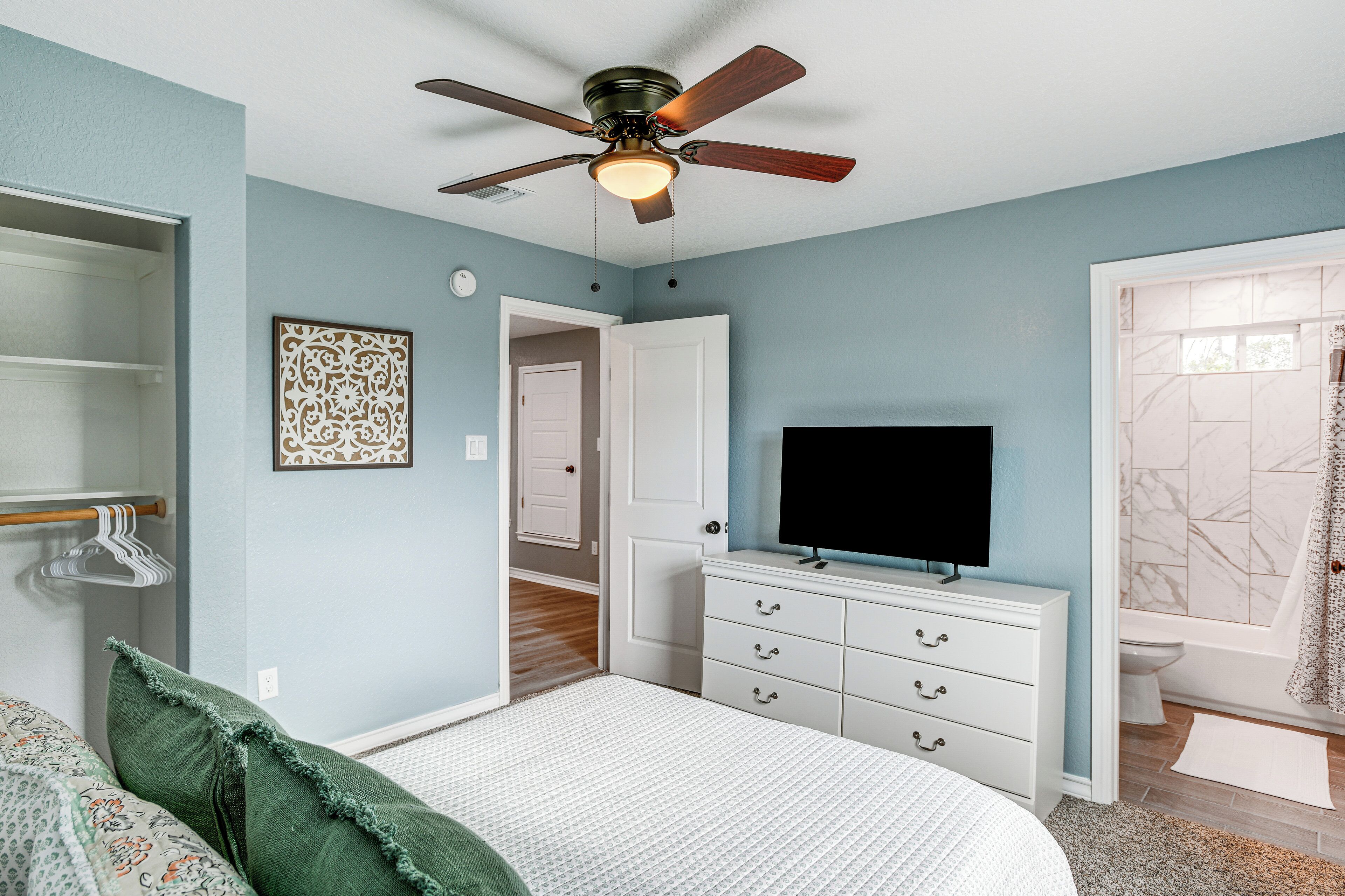 Quarto com cama, cômoda, televisão e ventilador de teto.