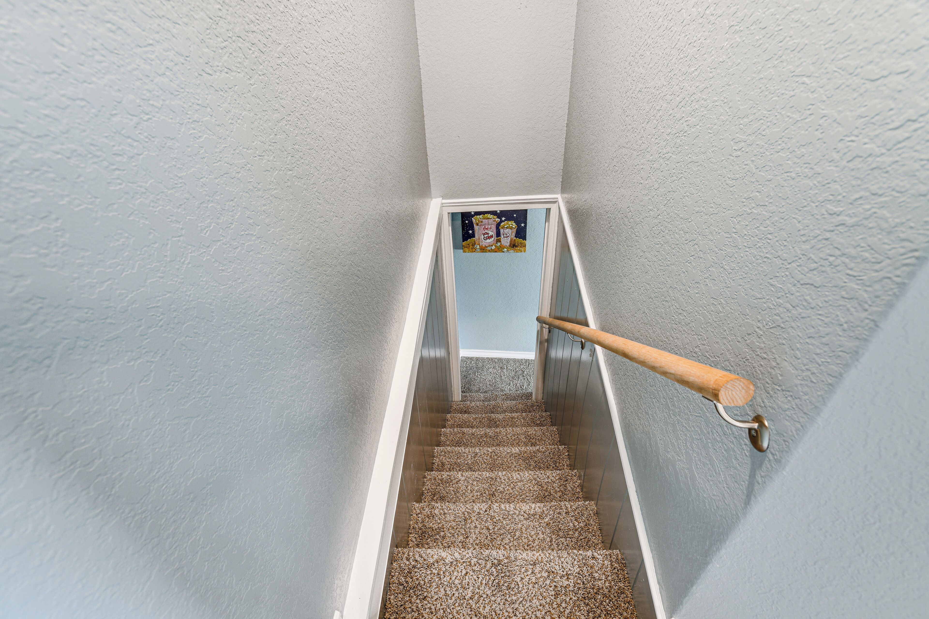A staircase with a wooden handrail, carpeted steps, and a framed picture at the top.