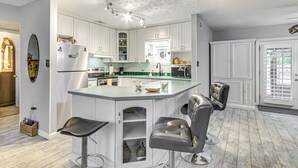 A modern kitchen with white cabinets, a central island with bar stools, and a ceiling fan. - Fort Walton Beach Home w/ Pool: 5 Mi to Beach! (Fort Walton Beach)