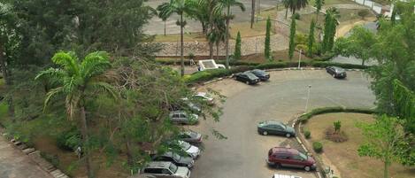 A parking area with multiple cars, surrounded by trees and a small building.