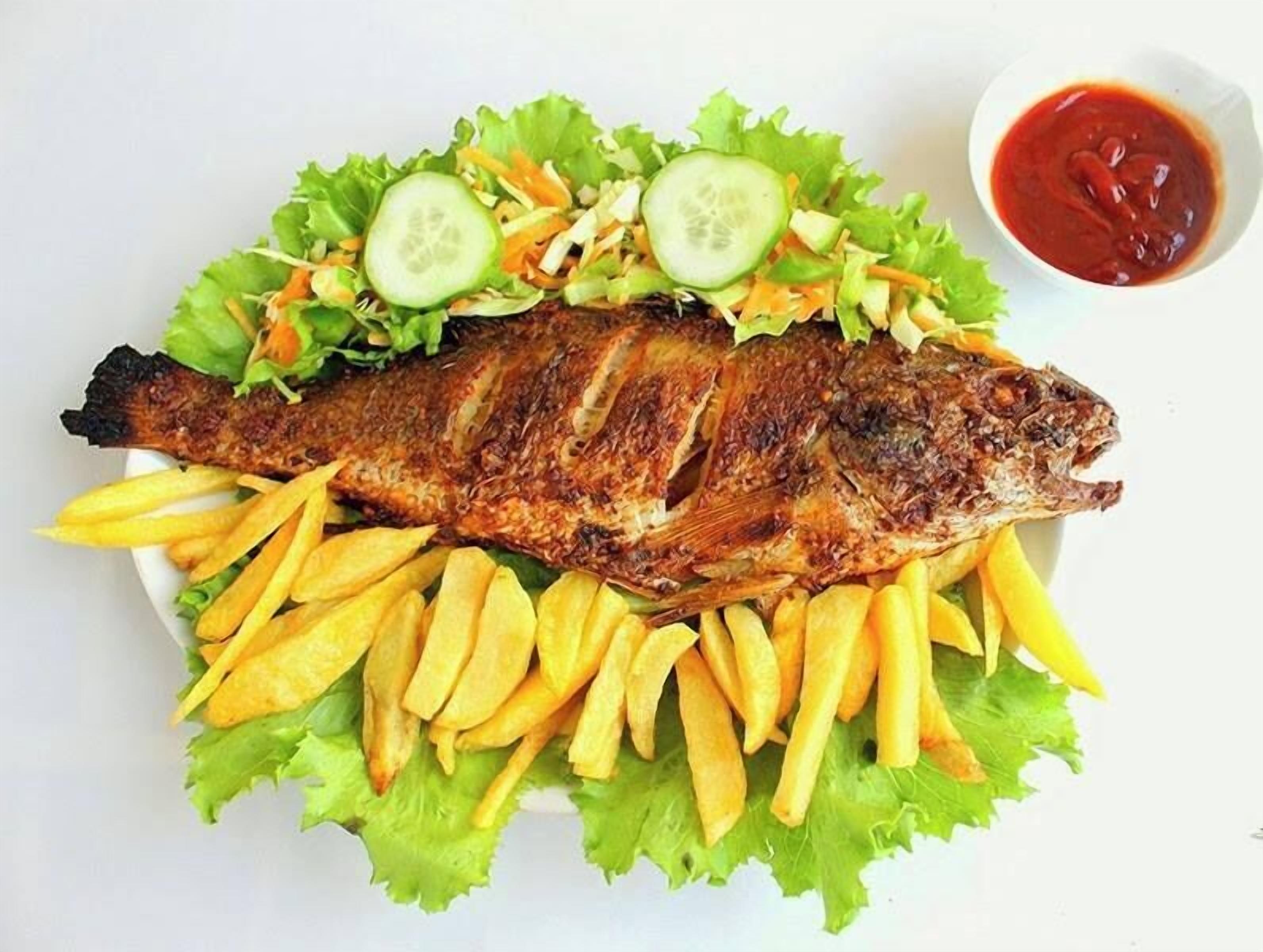 Un pescado a la parrilla con papas fritas y ensalada en un plato blanco.