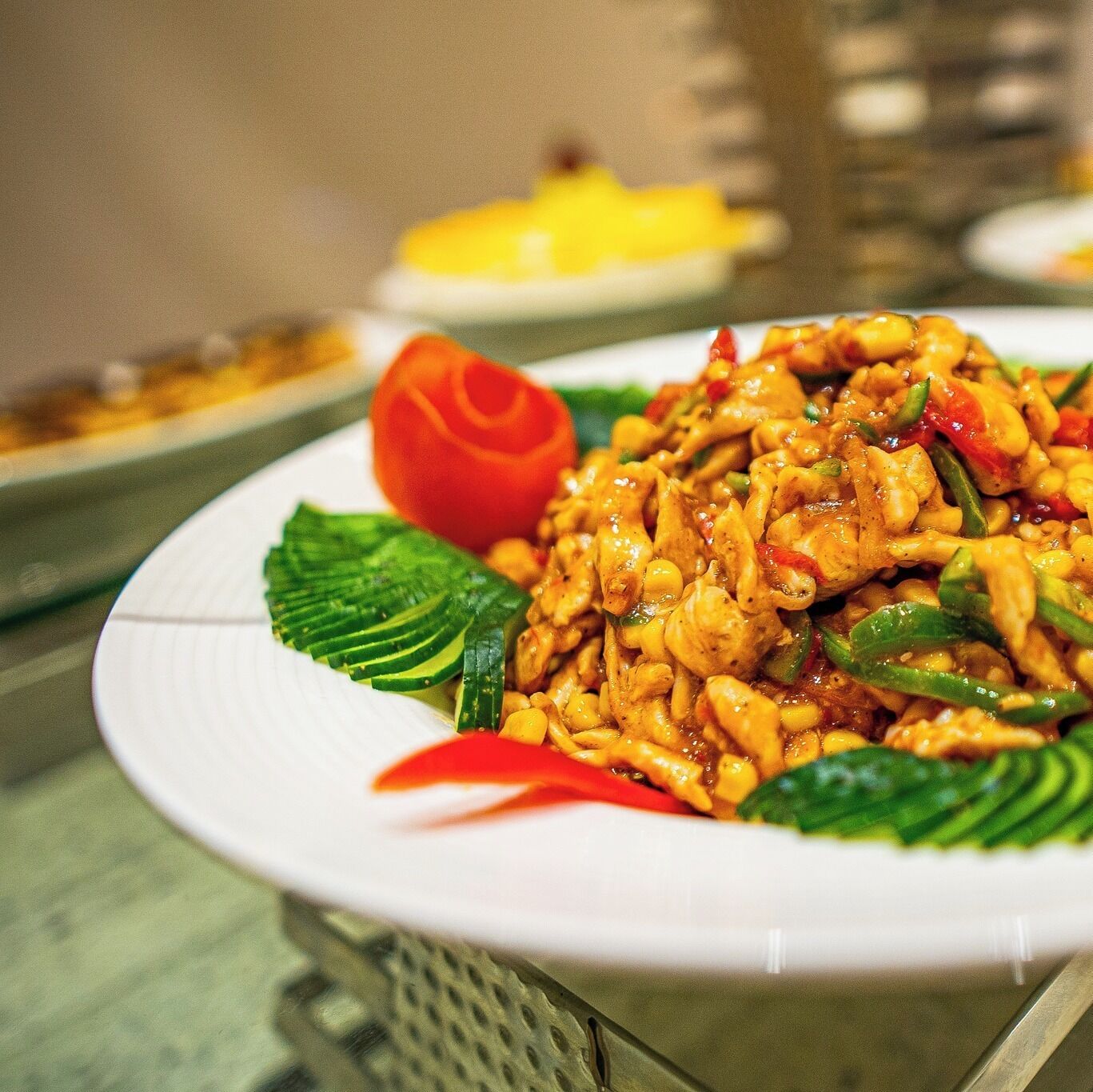 A plate of stir-fried chicken with vegetables and a decorative tomato on a white plate.