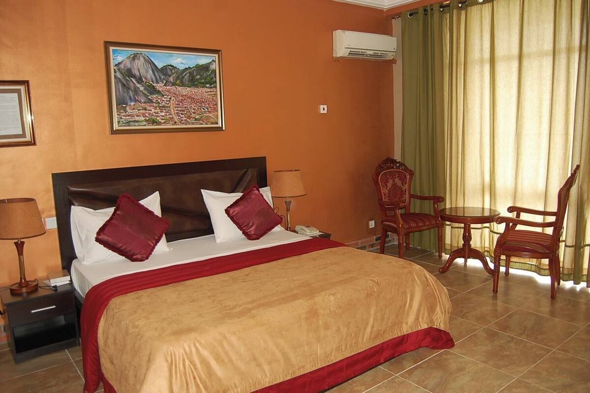 Una camera d'albergo con un letto grande, un quadro di un paesaggio montano, una sedia e un tavolo.