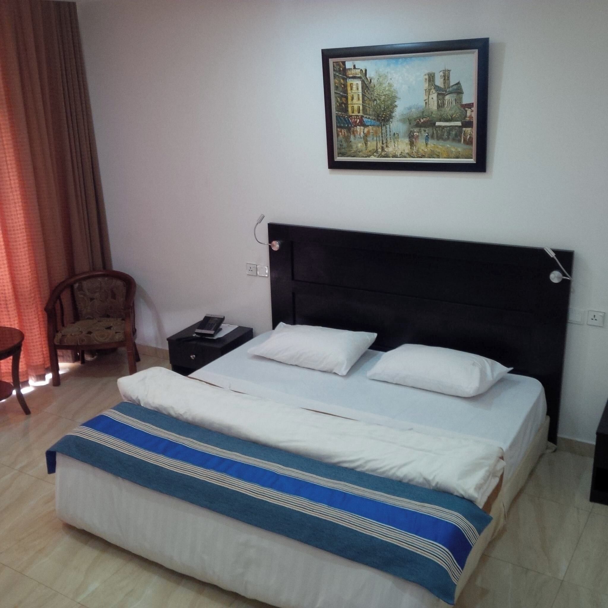Een hotelkamer met een bed, een nachtkastje, een stoel en een schilderij aan de muur.