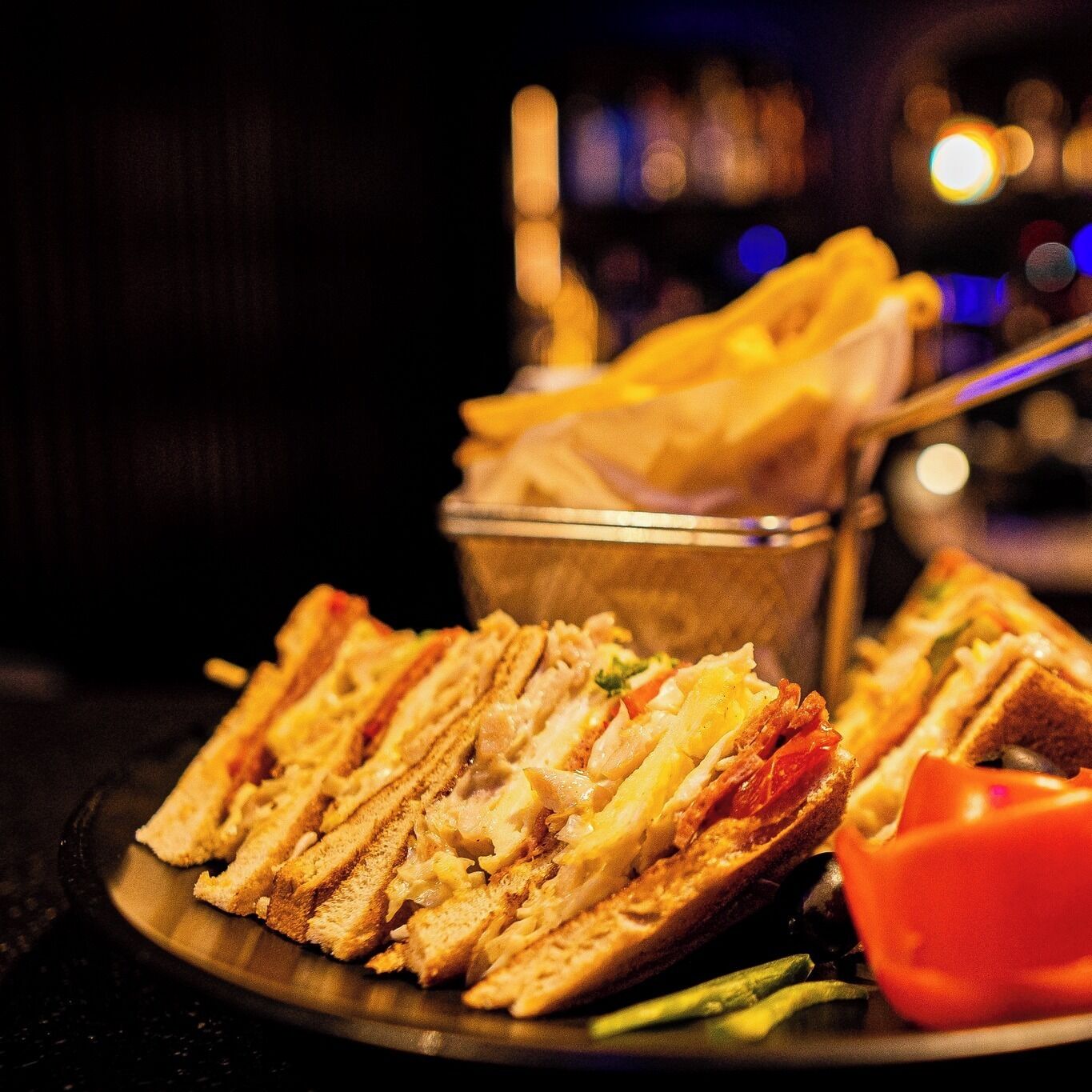 Une assiette avec un sandwich et des frites, un petit bol et une tomate, le tout posé sur une surface sombre.