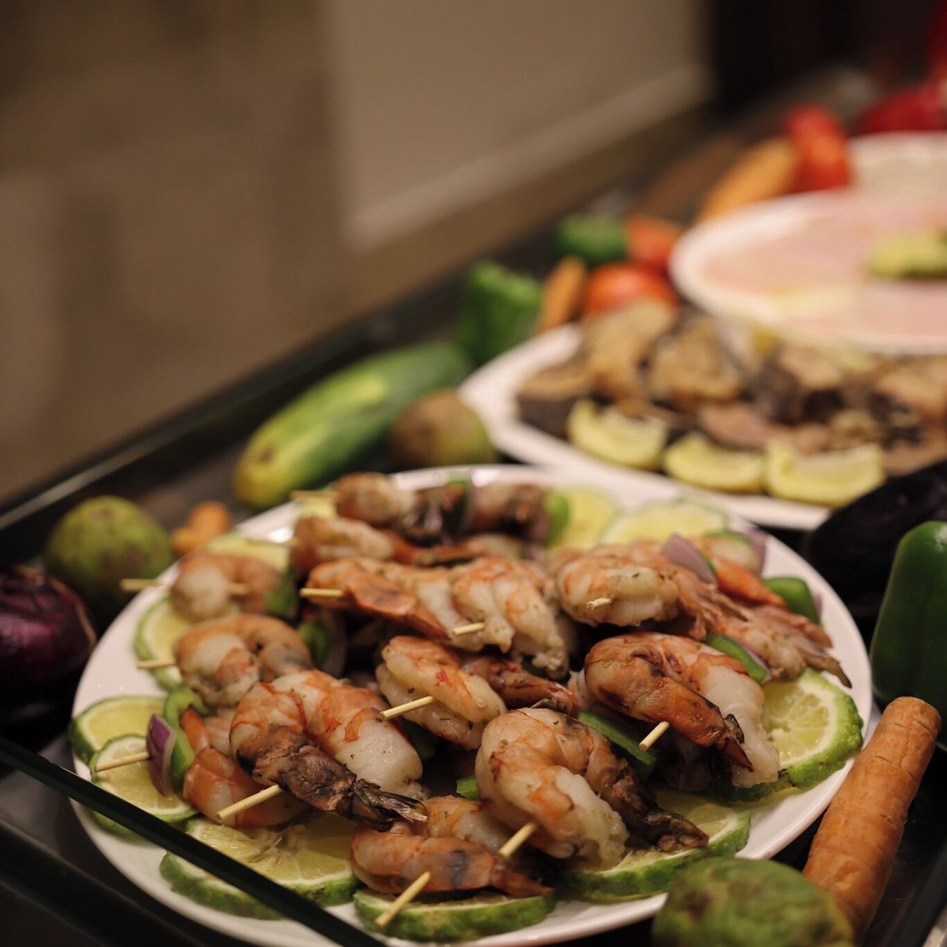 A buffet table with various dishes including shrimp skewers, vegetables, and other foods.