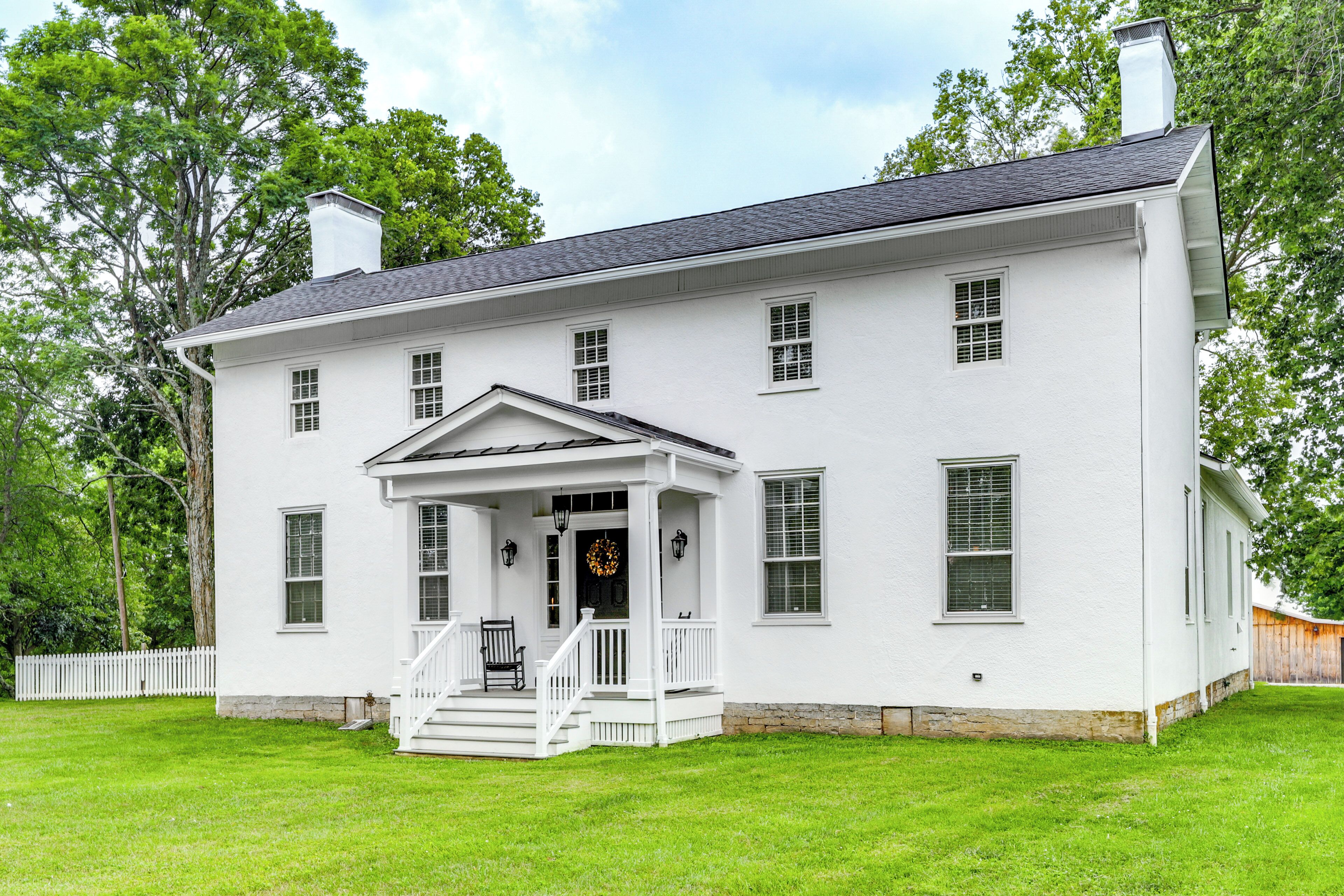 A white two-story house with a porch, multiple windows, and a chimney.