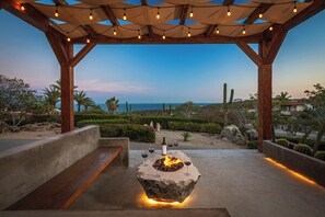 Relax by the fire pit in a serene garden setting, surrounded by lush greenery and ocean views.