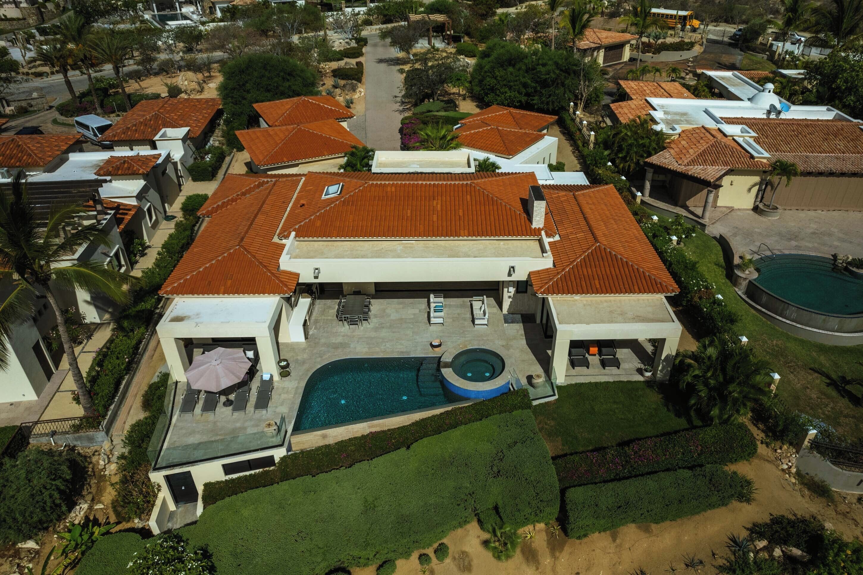 An aerial view of a residential area with multiple houses, a swimming pool, and well-maintained gardens.