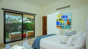 Una camera da letto con un letto grande, una porta scorrevole in vetro che dà su un patio e un quadro con un'auto gialla e la scritta “SUN SEA SURF”.
