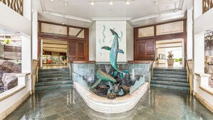 A lobby with a central fountain, a staircase, and a view of a store. - Ocean and Sunset Marina Views at the Ilikai Hotel w/Great Building Amenities (Honolulu)