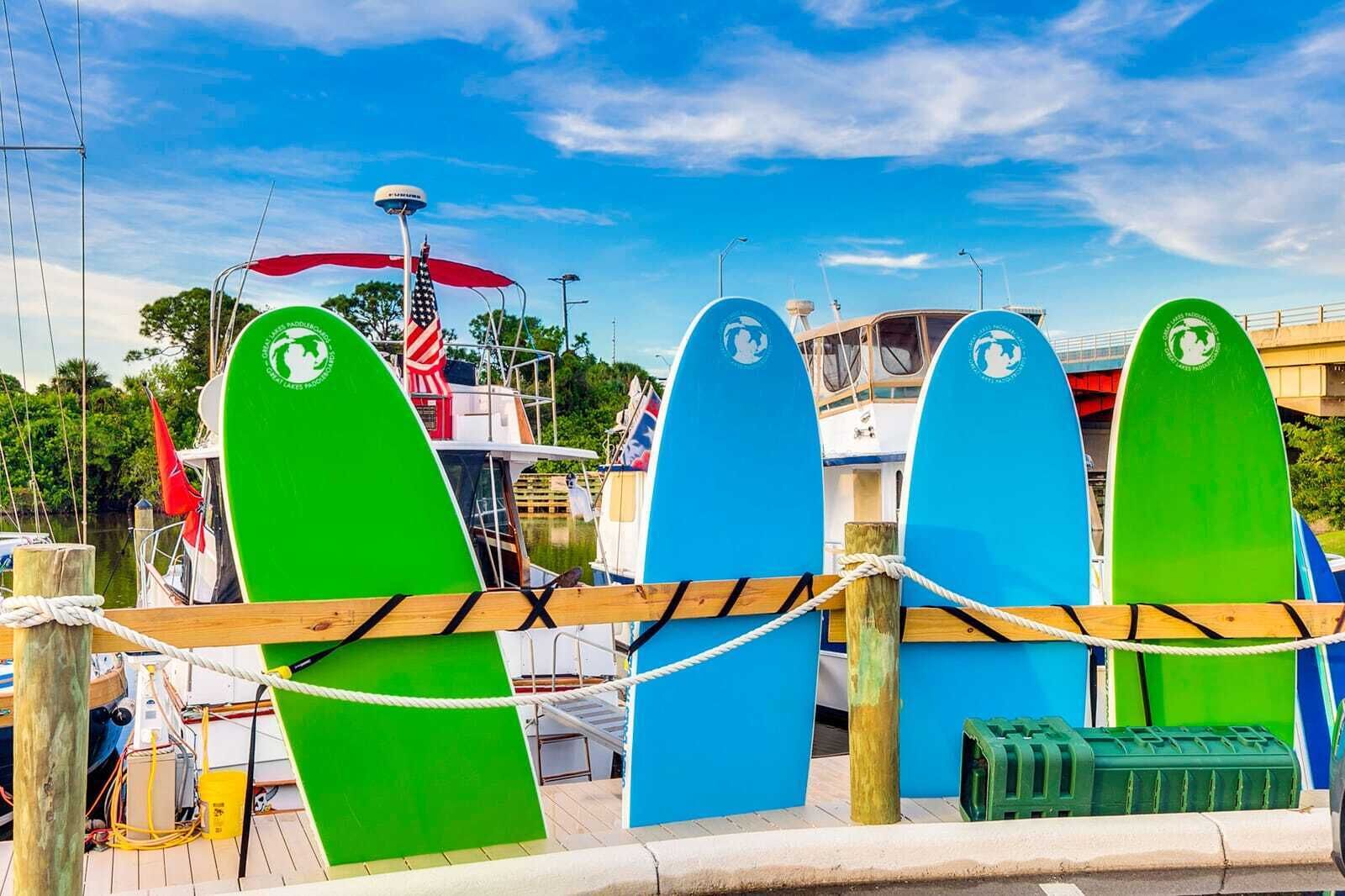 Een jachthaven met kleurrijke surfplanken langs de steiger, een boot met een Amerikaanse vlag, en een helderblauwe lucht.