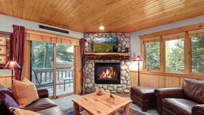 A cozy living room with a stone fireplace, leather furniture, and large windows offering a view of the outdoors. - Managed by Park City Lodging-Great Condo Near Canyons Village-Free Shuttle Route (Park City)