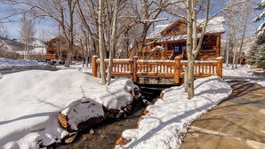 A wooden cabin with a stone foundation, surrounded by snow-covered ground and trees. - Managed by Park City Lodging-Great Condo Near Canyons Village-Free Shuttle Route (Park City)