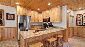 A kitchen with wooden cabinets, stainless steel appliances, granite countertops, and a bar area with stools. - Managed by Park City Lodging-Great Condo Near Canyons Village-Free Shuttle Route (Park City)