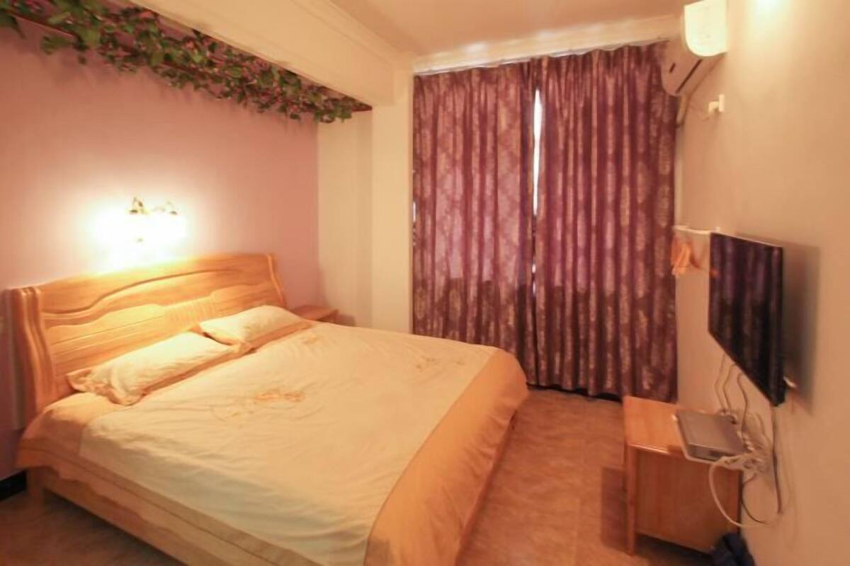 A bedroom with a bed, a bedside table, a TV, and a window with curtains.