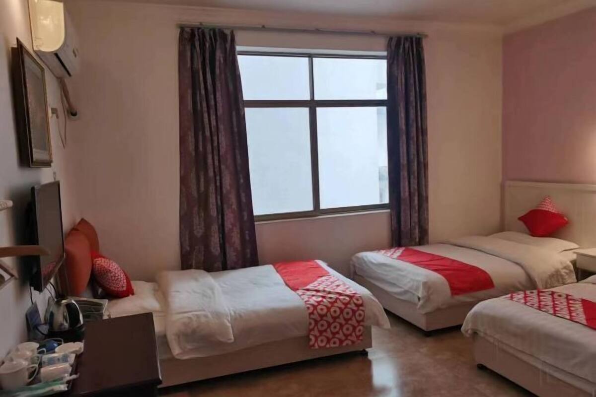 A hotel room with two beds, a desk, a chair, a TV, and a window with curtains.