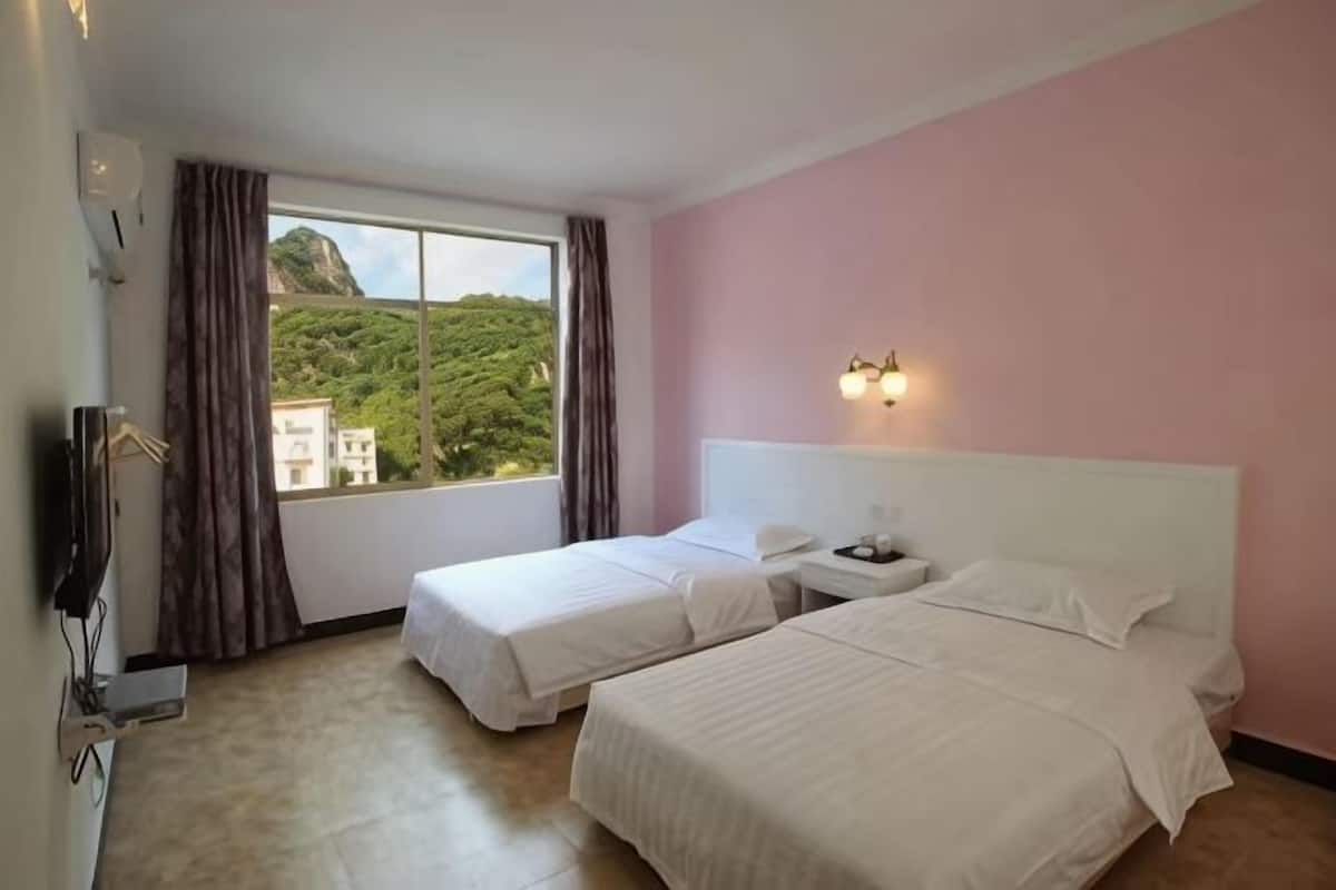 A hotel room with two beds, a window with curtains, a nightstand, and a wall-mounted light fixture.