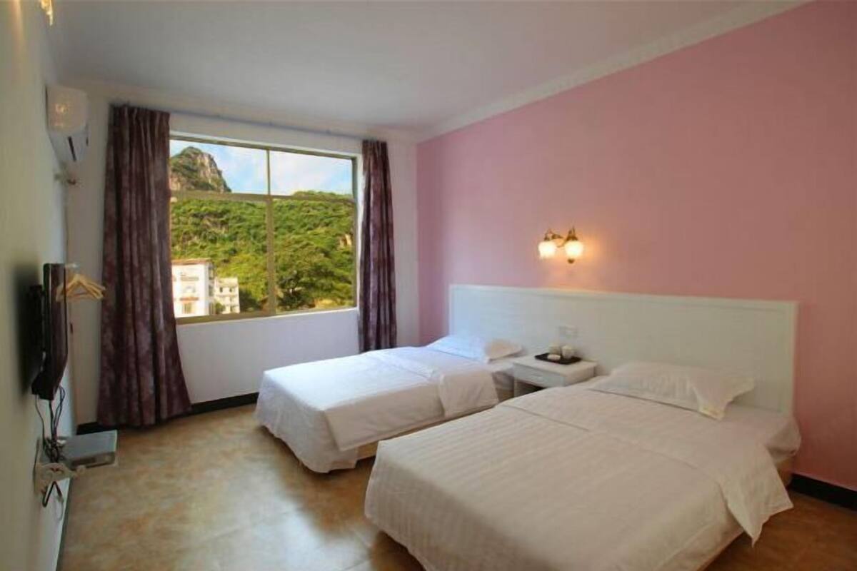 A hotel room with two beds, a window with curtains, a nightstand, and a wall-mounted light fixture.