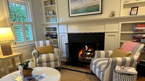 Un salon chaleureux avec une cheminée, des fauteuils à rayures, une table basse ronde et un pouf à rayures.