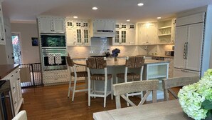Une cuisine moderne avec des meubles blancs, un îlot central doté de chaises et une table à manger.
