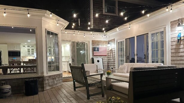 Une terrasse extérieure avec une plateforme en bois, un canapé blanc, une table à manger et des guirlandes lumineuses.