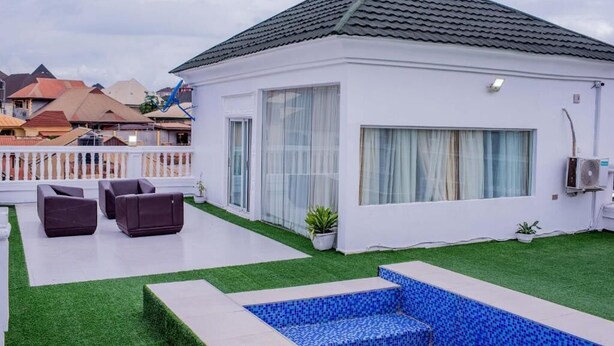A modern house with a white exterior, a tiled roof, and a small backyard with artificial grass and a blue-tiled pool. - MONDEESTARS LUXURY HOME (Ibadan)