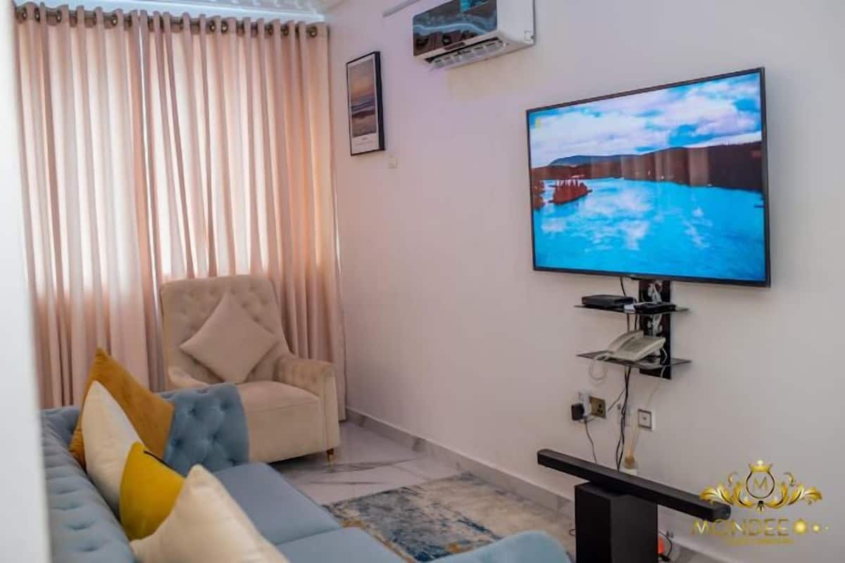 Una sala de estar con un sofá, un sillón, un televisor de pantalla plana y un aire acondicionado instalado.